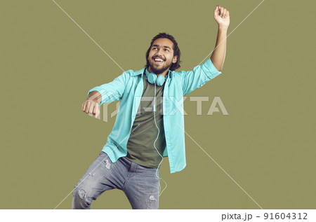 Cheerful funny indian man in headphones around his neck dancing and having fun on khaki background. Cheerful funny indian man in headphones around his neck dancing and having fun on khaki background. 91604312