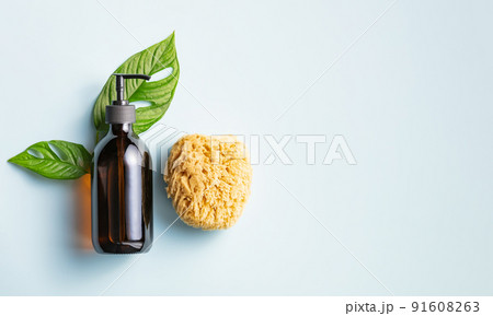 One cosmetic dark amber glass bottle with green plant and loofah on blue background One cosmetic dark amber glass bottle with green plant and loofah on blue background 91608263