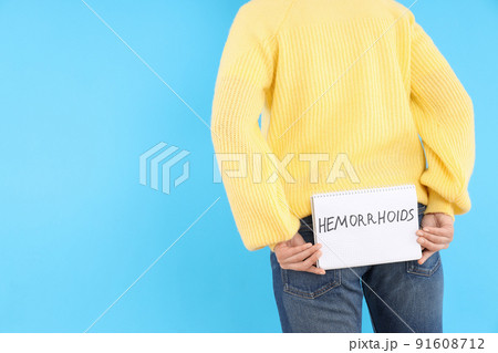 Woman holds text Hemorrhoids on blue background. Hemorrhoids concept 91608712