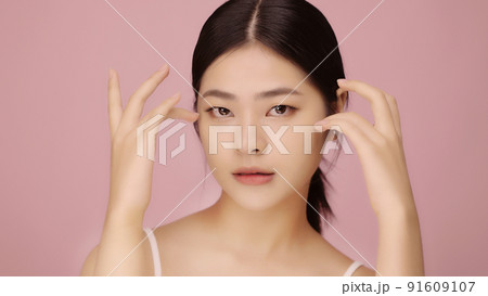 Close up face of beautiful young Asian woman with clear skin lifting eyes with finger on pink background. 91609107
