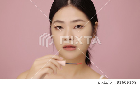 Close up face of beautiful young Asian woman applying lip on her lips on pink background. 91609108