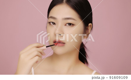 Close up face of beautiful young Asian woman applying lip on her lips on pink background. Close up face of beautiful young Asian woman applying lip on her lips on pink background. 91609109