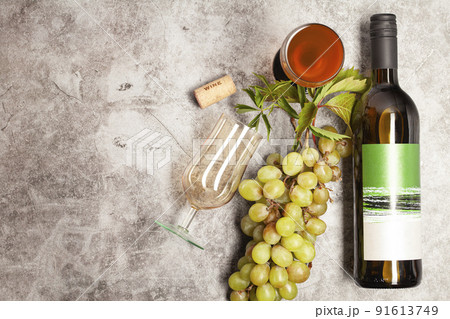 White wine bottle with bunch of grapes, glass on a dark background, top view. 91613749