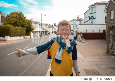 Funny kid boy in outstretched hand brakes car. Child raising thumb up to catch the car. Hailing taxi concept. kid is stopping a car standing on the road in center of city 91615664