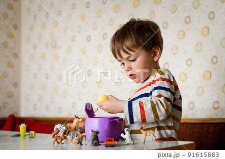 Funny kid eat boiled egg with hands. Eating vegetable at home kitchen. Child play toys animals while eating lunch in kindergarten or at home 91615683