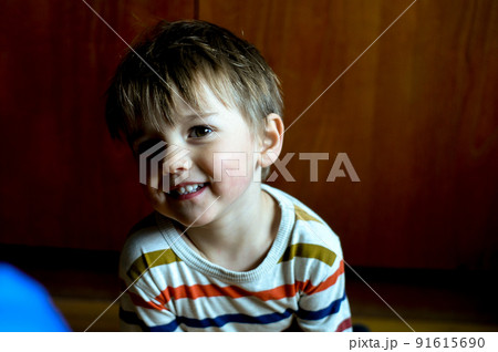Face of nice baby child. Portrait of happy joyful laughing beautiful little boy smiling. Funny kid playing while sitting on wooden floor in the room. 91615690