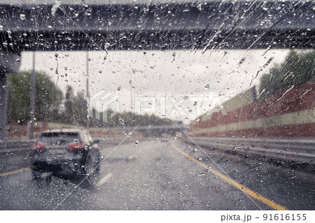Road view through windshield car window with going rain drops during driving at speed. Unfocused highway. Autumn 91616155