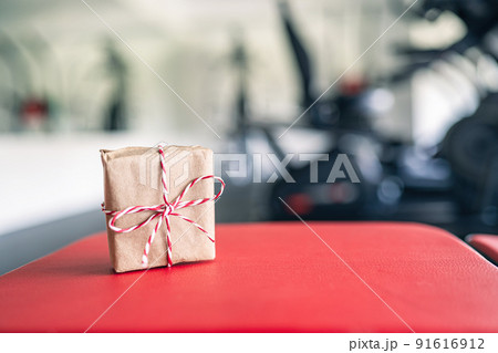 Small gift box with bow in the gym opposite the equipment and jogging simulators. Symbol and concept of discount offer on Christmas and New Year. Copy space. Small gift box with bow in the gym opposite the equipment and jogging simulators. Symbol and concept of discount offer on Christmas and New Year. Copy space. 91616912