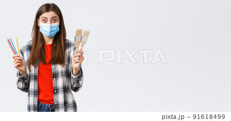 Social distancing, leisure and hobbies on covid-19 outbreak, coronavirus concept. Excited cheerful girlfriend suggest drawing together, holding painting brushes and colored pencils, wear medical mask 91618499