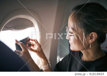 asian woman passenger taking a photo with cellphone through airplane window 91618605