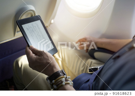 asian man male passenger sitting in cabin of airplane reading ebook using e-reader 91618623