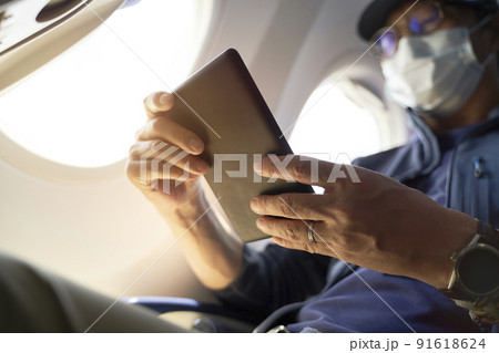 asian man male passenger sitting in cabin of airplane reading ebook using e-reader asian man male passenger sitting in cabin of airplane reading ebook using e-reader 91618624