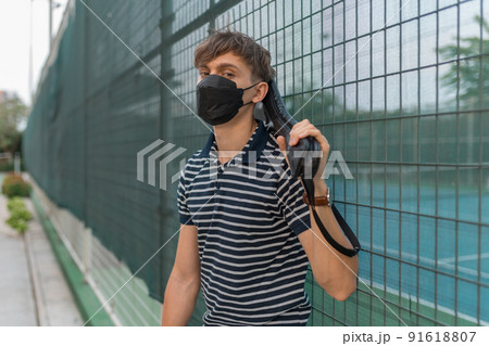 Young man wearing black face mask standing on the tennis court and holding tennis racket. High quality photo 91618807
