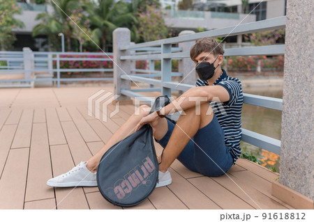 Young caucasian man wearing black face mask sitting and holding tennis racket. High quality photo 91618812