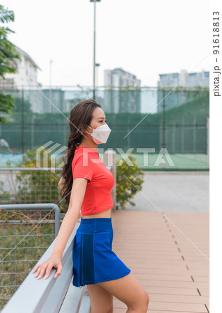 Pretty young asian woman wearing tennis outfit face mask standing near the tennis court. High quality photo 91618813