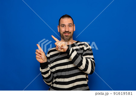 Happy smiling 40 year old man in ryas sweater pointing with index fingers to the side at mock up workspace area isolated on blue color background studio portrait. People lifestyle concept. 91619581
