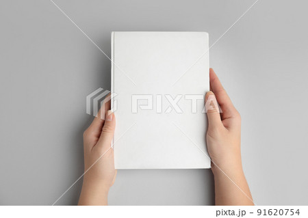 Woman holding book with blank cover on grey background, top view Woman holding book with blank cover on grey background, top view 91620754