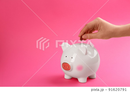 Woman putting coin into piggy bank on pink background, closeup. Space for text Woman putting coin into piggy bank on pink background, closeup. Space for text 91620791