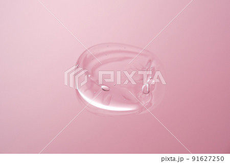 Drop of cosmetic transparent gel on a pink background. The texture of the serum, heir gel or hyaluronic booster. Drop of cosmetic transparent gel on a pink background. The texture of the serum, heir gel or hyaluronic booster. 91627250