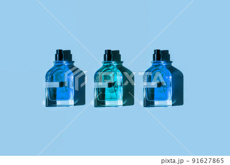 Three different perfume bottles on a pastel blue background in the sunlight. Flat lay, top view. Luxury presentation mockup. Cyan and blue samples of aroma water 91627865