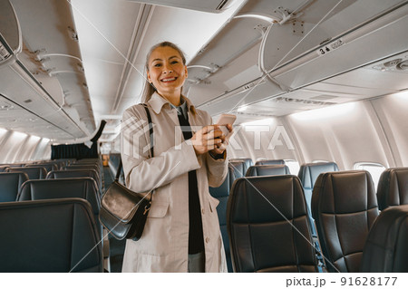 Smiling passenger with phone stands in cabin of aircraft during landing in airport Smiling passenger with phone stands in cabin of aircraft during landing in airport 91628177