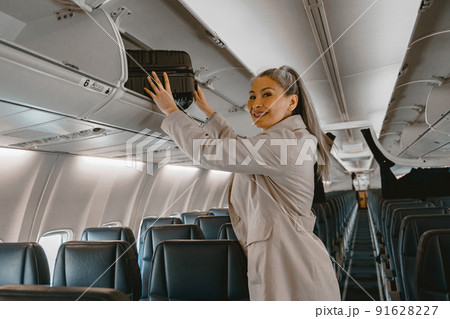 Asian Woman traveler putting luggage into overhead locker on airplane during boarding Asian Woman traveler putting luggage into overhead locker on airplane during boarding 91628227