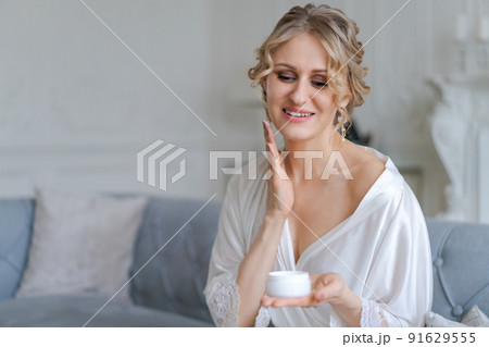 Young happy woman holding cosmetic face cream and smiling while applying cream 91629555