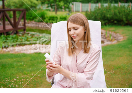 Young woman applies cream to her face while sitting in garden in country house Young woman applies cream to her face while sitting in garden in country house 91629565