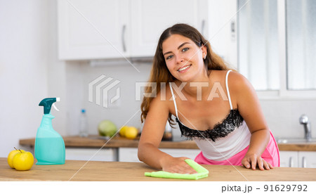 Cheerful young woman washing kitchen table at home Cheerful young woman washing kitchen table at home 91629792