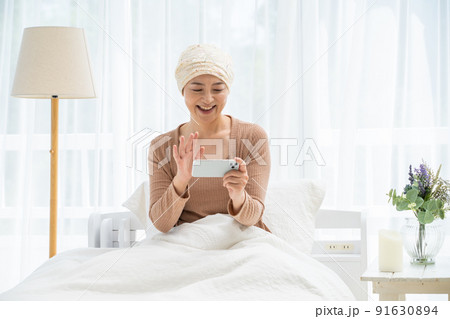ベッドでスマホを見る医療用帽子をかぶったミドル女性 91630894
