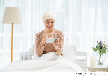 ベッドでスマホを見る医療用帽子をかぶったミドル女性 91630895
