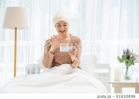 ベッドでスマホを見る医療用帽子をかぶったミドル女性 91630896
