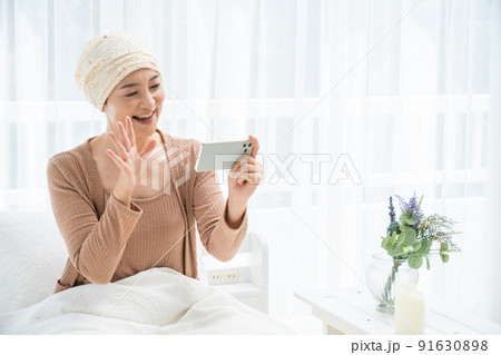 ベッドでスマホを見る医療用帽子をかぶったミドル女性 91630898
