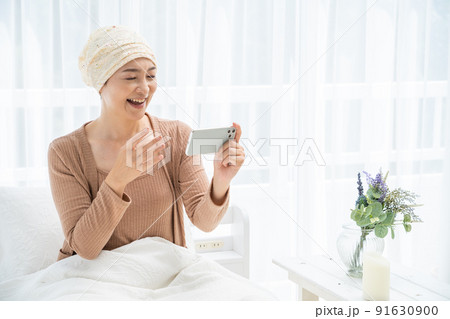 ベッドでスマホを見る医療用帽子をかぶったミドル女性 91630900