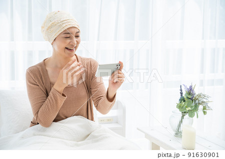 ベッドでスマホを見る医療用帽子をかぶったミドル女性 91630901