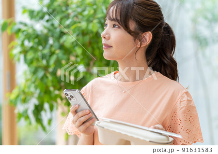 お弁当とスマホを持つ若い女性 91631583