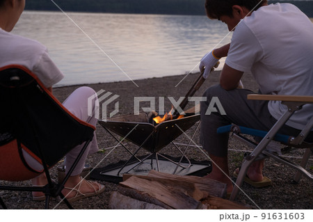 夕焼けを見ながら焚き火をするカップル 91631603