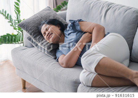Woman suffering from stomachache lying down on the sofa at home. abdominal pain, Gastritis, Period, menstruation. Woman suffering from stomachache lying down on the sofa at home. abdominal pain, Gastritis, Period, menstruation. 91631615