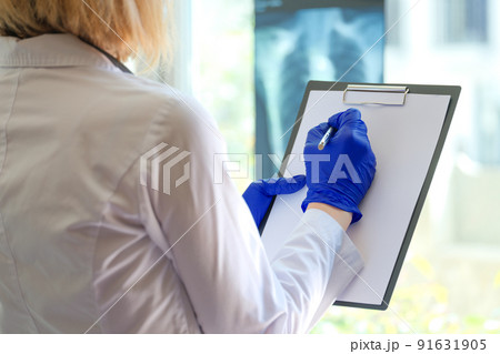 Practitioner with clipboard filling form of patient or writing description of xray Practitioner with clipboard filling form of patient or writing description of xray 91631905