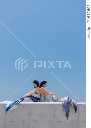 夏の海の海岸でマーメイドを練習して遊んでいる二人の女性の姿 91632605