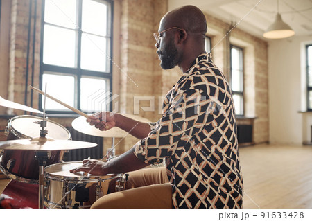 Young African drummer playing at drums set during rehearsal at musical studio Young African drummer playing at drums set during rehearsal at musical studio 91633428