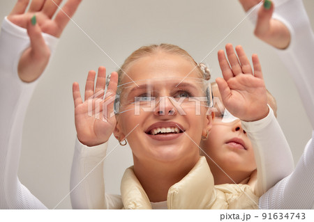 A young woman with her little daughter in a white high-tech clothes wearing smart glasses and pressing by hands up against a holographic screen A young woman with her little daughter in a white high-tech clothes wearing smart glasses and pressing by hands up against a holographic screen 91634743