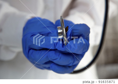 The doctor's hands in blue gloves holding a stethoscope. Close-up. The doctor's hands in blue gloves holding a stethoscope. Close-up. 91635871