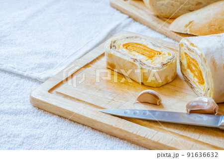 Sliced roll of Armenian pita bread with carrot filling on a wooden board. 91636632
