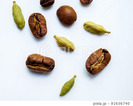 Coffee beans and cardamom grains are scattered on a white glossy surface. Coffee beans and cardamom grains are scattered on a white glossy surface. 91636740