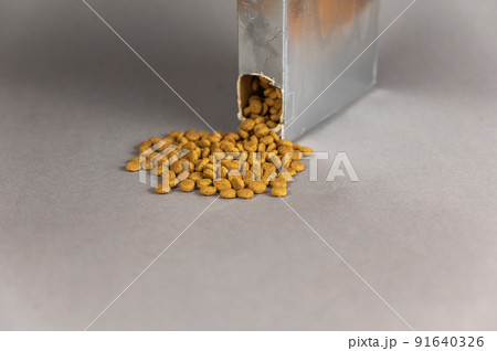 A silver rectangular box against a gray background. Pet food spilling out of the hole. Dry pelleted food. Pet food. Selective focus. 91640326