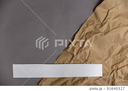 Wrapping paper and a white diagonal stripe against the gray background. Crumpled sheet of light brown paper lies on gray surface. Top view. Space for text and design elements. 91640327