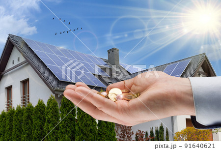Hand with money against background of house with installed solar panels. Renewable energy and saving money. Conceptual image Hand with money against background of house with installed solar panels. Renewable energy and saving money. Conceptual image 91640621