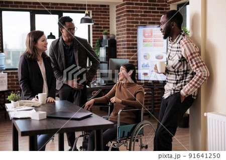 Happy businesspeople talking on break in disability friendly office, laughing with impaired asian woman. Female wheelchair user with physical health condition chatting with work colleagues. Happy businesspeople talking on break in disability friendly office, laughing with impaired asian woman. Female wheelchair user with physical health condition chatting with work colleagues. 91641250