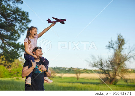 Cute girl riding on father's shoulder playing with toy airplane 91643371